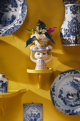One of Danish ceramics brand Bjørn Wiinblad's colourful handpainted ladies with hats vases displayed against a yellow background