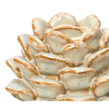 Close-up detail of a ceramic sculptural candle holder shaped like a pine cone featuring a glossy off-white glaze with subtle brown speckling and warm tan edges, set against a plain white background