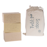 Stack of 3 carrot, almond and apricot kernel soap bars by Iris Hantverk beside a drawstring bag on a white background.