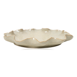 A scalloped ceramic plate in a speckled beige glaze from Broste Copenhagen, shown from a side angle on a white background