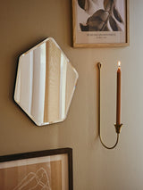 A wall-mounted metal candle holder with a brass finish, holding a single brown taper candle in a hallway setting