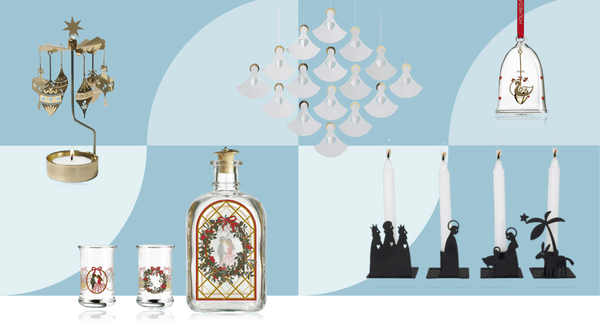 Traditional Scandinavian Christmas decorations including gold rotary candle holder, paper angel mobile, glass bell ornament, Holmegaard collectible glasses and schnapps bottle, white candles and black silhouette nativity scene on light blue background