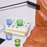 Blue and green glass Kastehelmi candle holders by Iittala Finland with a lit candle inside with books