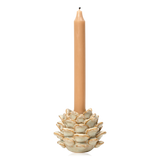 A tall, slim tan candle standing in a sculptural pinecone-shaped holder with a warm off-white glaze and subtle gold-toned edging, isolated on a white background