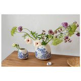 Two white ceramic vases by Arabia Finland with blue floral designs and featuring Moomin characters on a wooden surface 
