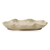 An oval-shaped ceramic serving platter from Broste Copenhagen with a wavy scalloped rim, featuring a speckled beige glaze on a white background, side angle.