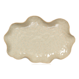 An oval-shaped ceramic serving platter from Broste Copenhagen with a wavy scalloped rim, featuring a speckled beige glaze on a white background.