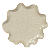 A scalloped ceramic plate in a speckled beige glaze from Broste Copenhagen, shown from a top-down view on a white background.