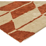 close-up detail of A rectangular rug by Broste Copenhagen with a geometric chevron pattern in terracotta orange and cream, shown flat against a white background.