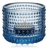 Blue glass Kastehelmi candle holder by Iittala Finland with a lit candle inside on a white background
