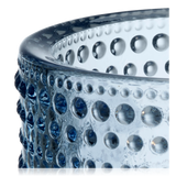detail of Blue glass Kastehelmi candle holder by Iittala Finland with a lit candle inside on a white background