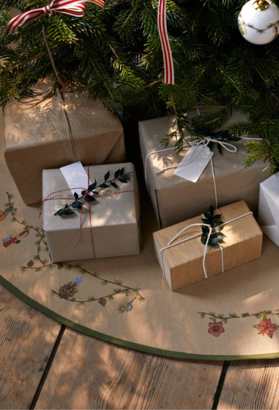 Gifts wrapped in brown and white paper under a nordic Christmas tree on a decorative Scandinavian style mat.